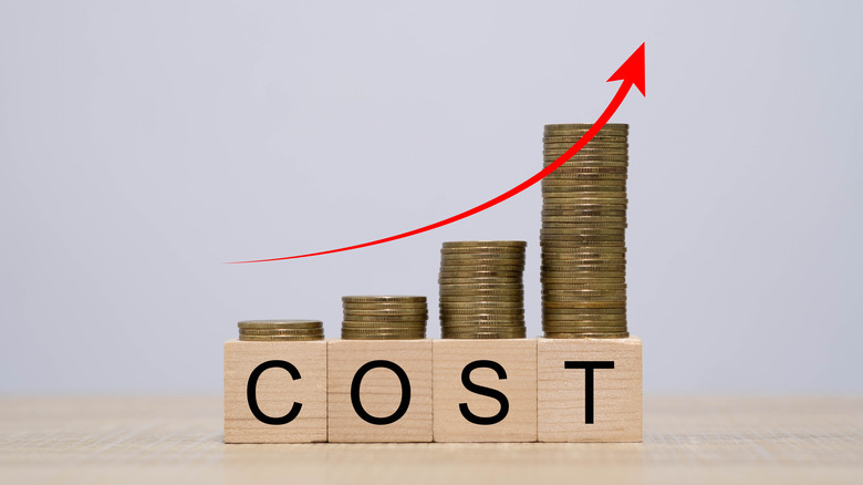 An artistic image of increasing costs depicted by stacks of coins getting larger on wooden blocks spelling out the word cost