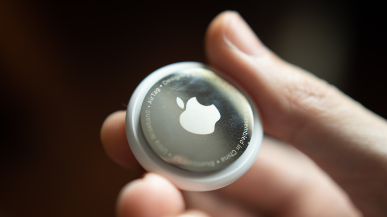 A person holding Apple's AirTag coin shaped Bluetooth tracker in their hands for pairing with iPhone.