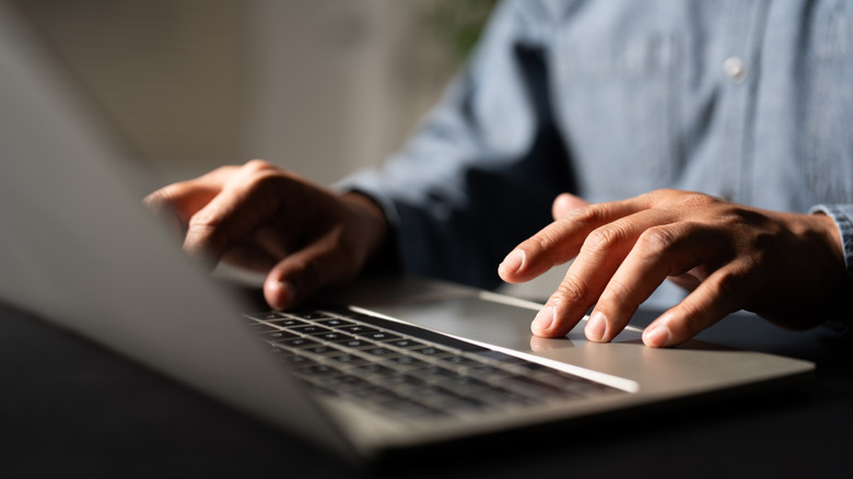 person working on a laptop with one hand on the keyboard and another on the touchpad