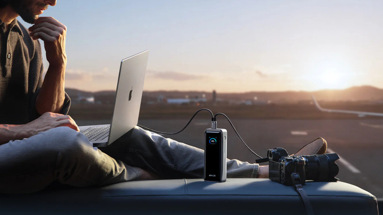 Man using Anker powerbank to charge macbook and camera outdoors with sunset in the horizon