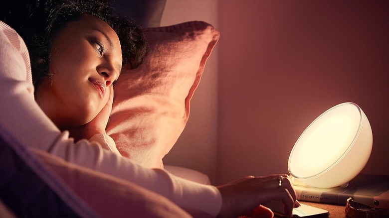 A person using a Philips Hue Go portable smart light on a bedside table.
