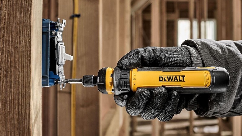 A gloved hand using the DeWalt FlexDrive cordless screwdriver on a light switch.