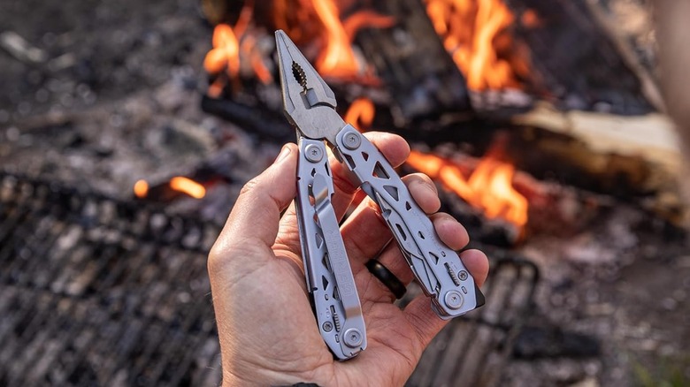 A hand holding the Gerber Suspension NXT multi-tool over a blurry campfire.