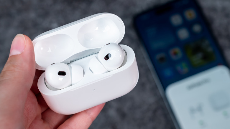 A person holding a pair of Apple AirPods Pro 2 in their charging case.