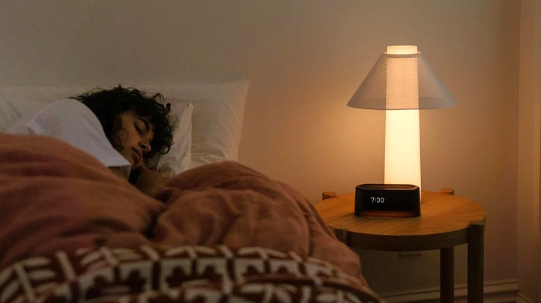 Loftie Alarm Clock on a nightstand with a light in view and a person sleeping.