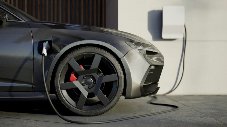 Front of electric vehicle visible and plugged in to charge from wall adapter.