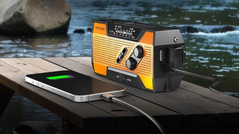 The FosPower Emergency Weather Radio (Model A1) on top of a picnic bench with a phone plugged into it.