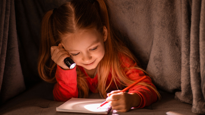 Little girl drawing by flashlight under covers