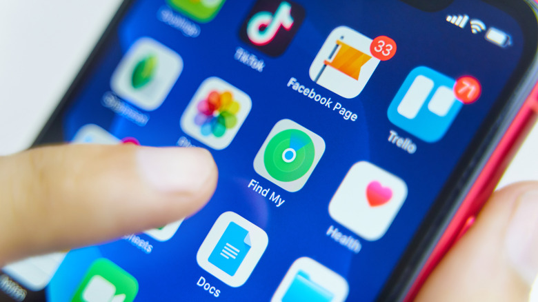 A finger pointing to the Find My app on iPhone.