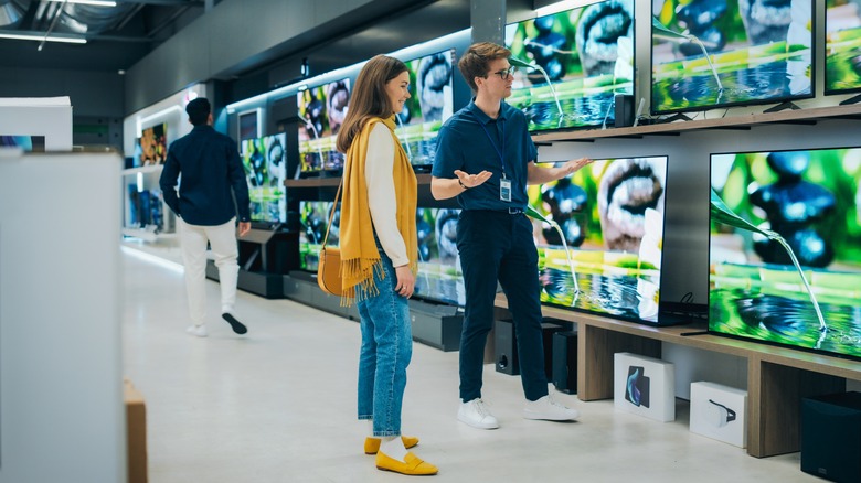 Sales associate showing TVs to customer in store.