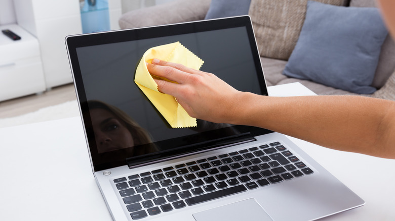 Woman cleaning a laptop screen with a microfiber cloth.