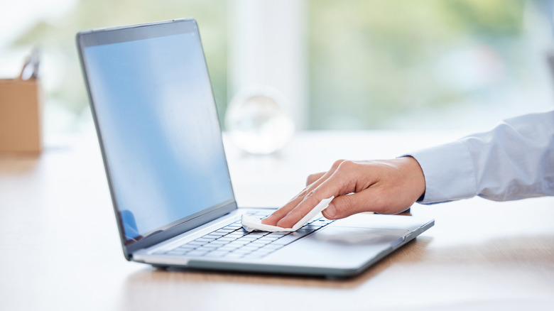 A man's hand cleaning a laptop keyboard with a cloth.