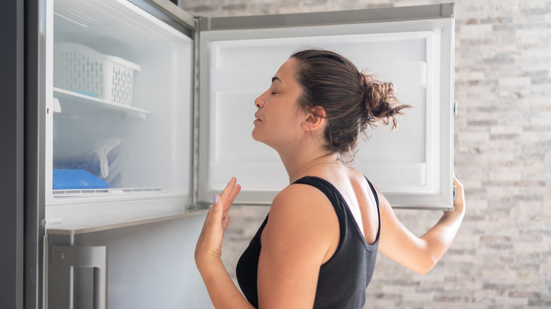 Woman trying to cool down by placing her body in front of an open freezer.
