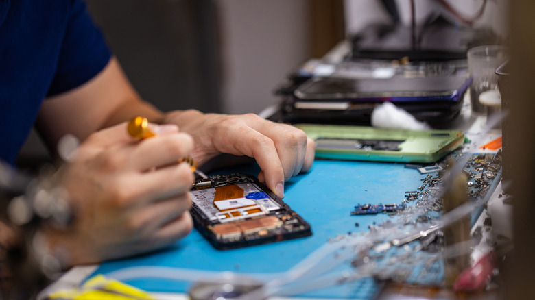 A person repairing a smartphone on an electronics work bench