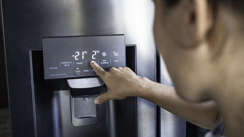 A person tapping the control panel of a smart refrigerator to adjust its settings