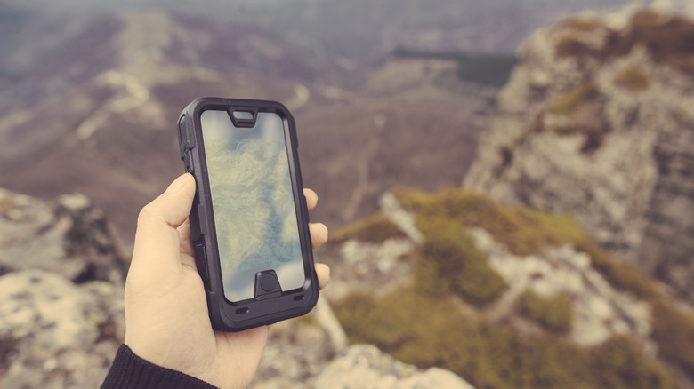 person holding a smartphone in a rugged case while hiking