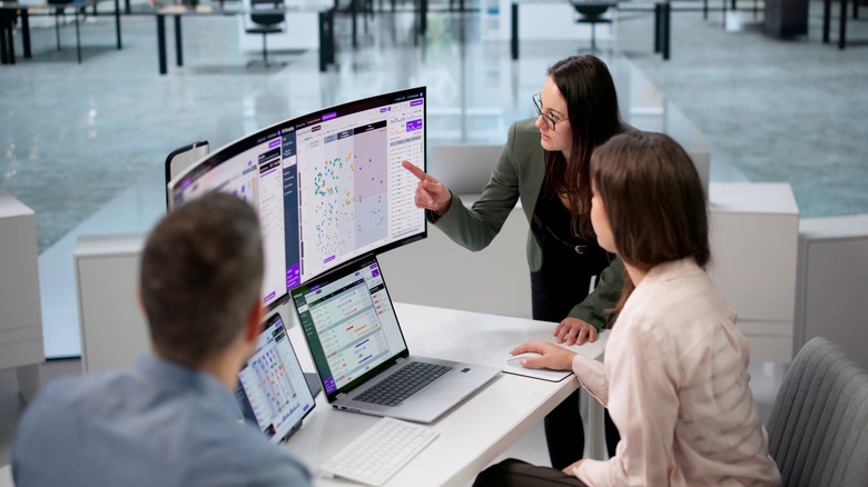 Three people at a desk with an ultrawide monitor and laptop