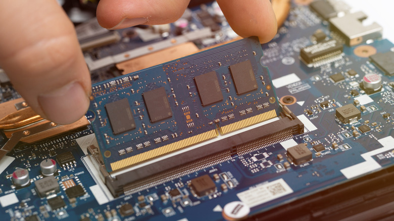 A stick of laptop RAM being inserted into its slot on a blue motherboard