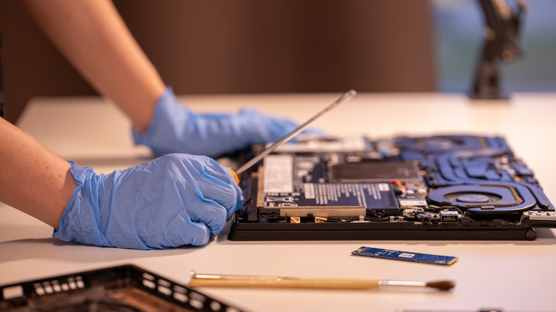 Two gloved hands placed beside an open laptop with internal components exposed