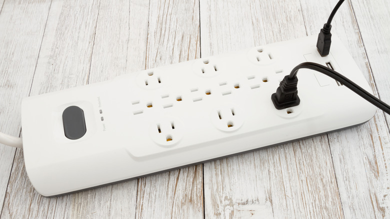 Surge protector on the floor with multiple electronics plugged in.