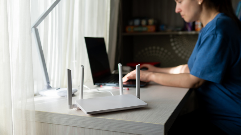 Wireless router on a desk with a person in the background using their laptop.