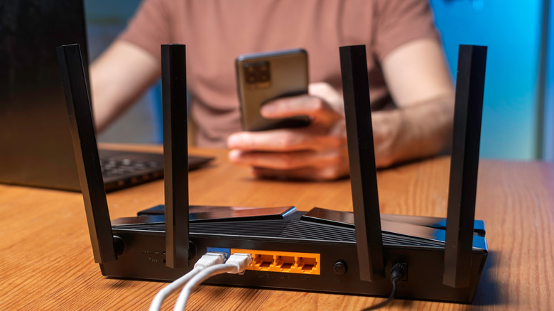 Wireless router on desk with person in background using phone and laptop.