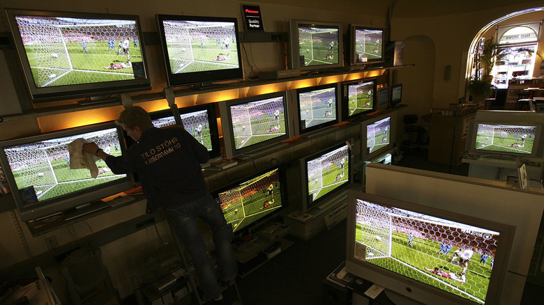 A person cleaning a number of TV screens displaying a soccer game