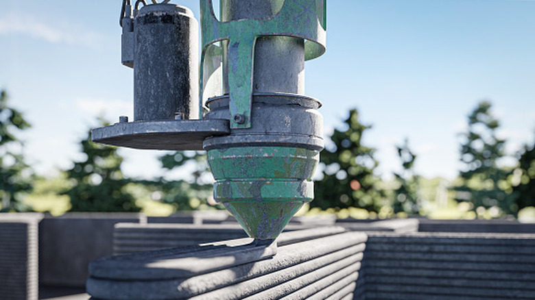 Industrial 3D printer nozzle depositing thick layers of concrete outdoors.