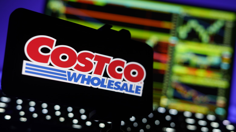 A cellphone displaying the Costco Wholesale logo, behind the device seems to be a number of graphs, though they are too blurred to get details