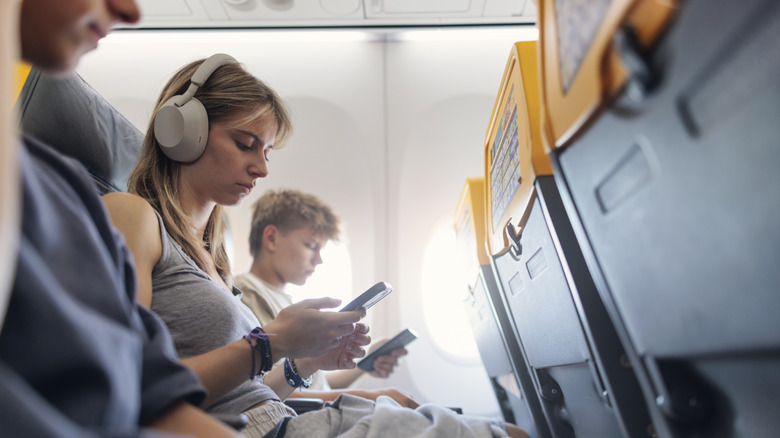 People using phones and electronic devices while seated in a plane.