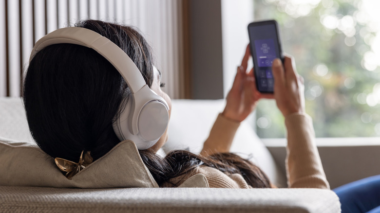 A woman listening to music on her phone wearing wireless headphones.