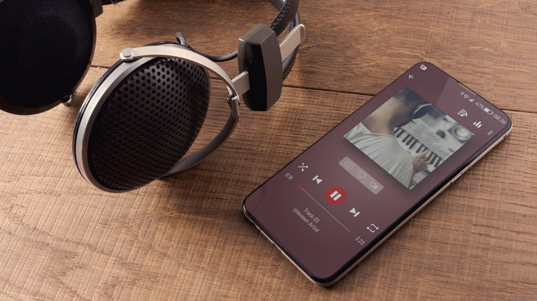 Premium headphones next to a phone that's playing audio, both on a wooden surface.