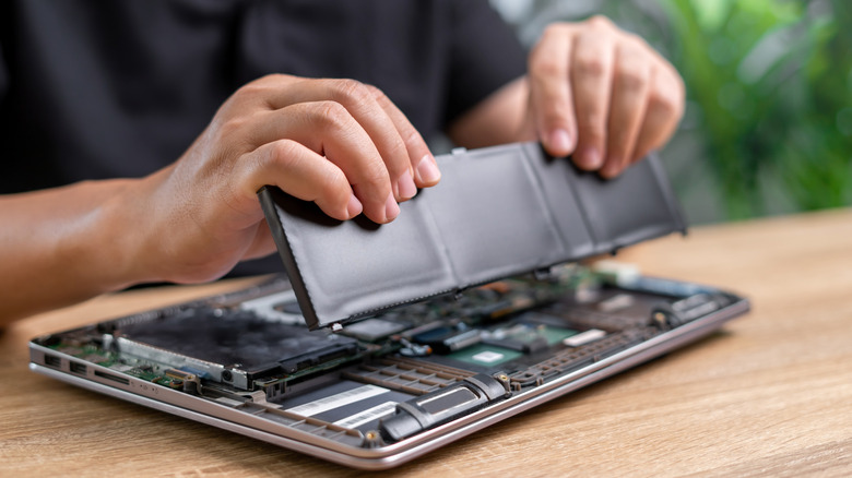 a person repairing and replacing a laptop battery component in a laptop
