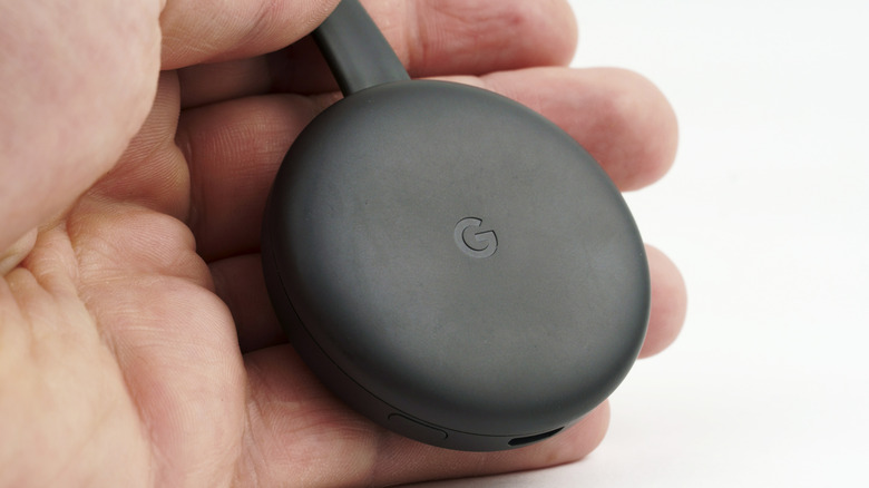 A zoomed image of a person's hand holding a Google Chromecast
