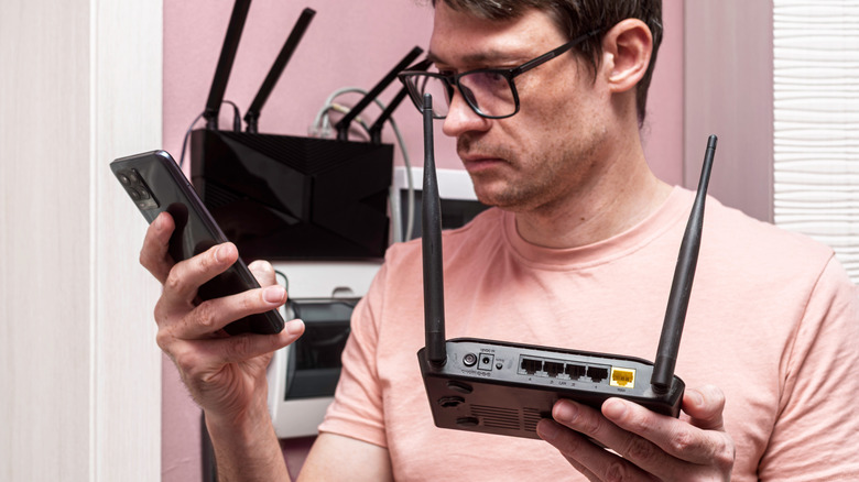 Person holding a smartphone and a Wi-Fi router