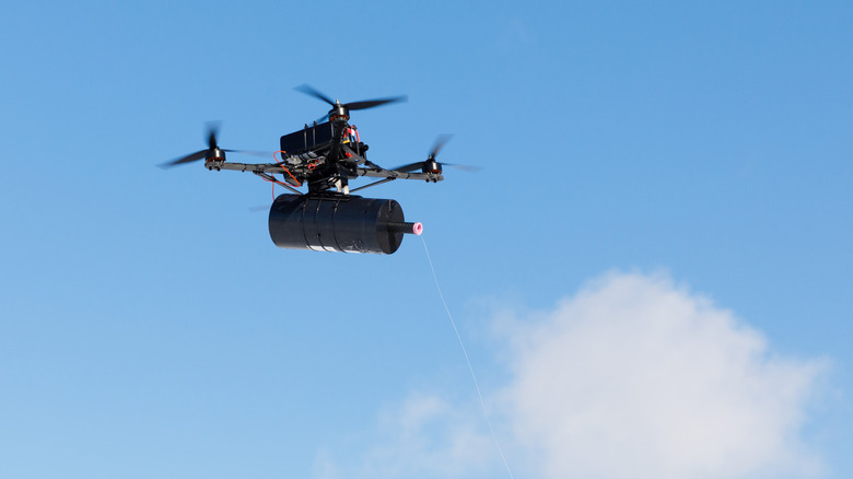 A fiber-optic drone flying, with a spool attached.