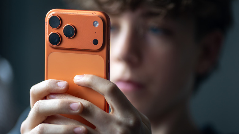 Young boy in the background looking at apps on orange smartphone