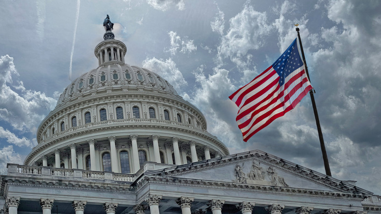 The US Capitol Building with the American flag against a cloudy scky