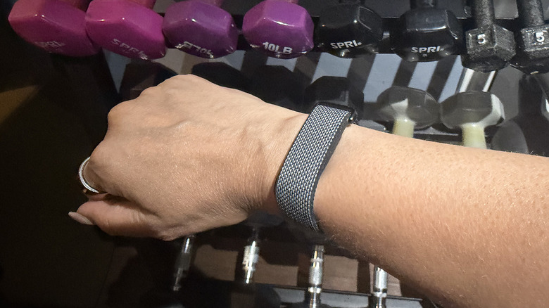 Fitbit Air on a wrist with dumbbells on a rack in the background.