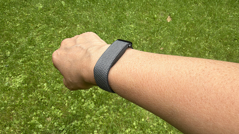 A Fitbit Air on a wrist with green grass in the background.