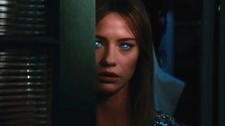 Sara standing behind a door in 