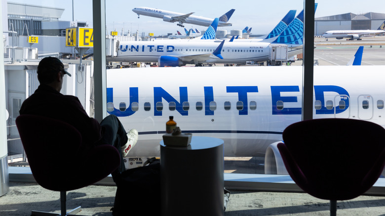 United Airlines planes on the ground seen through a window, with one taking off in the background