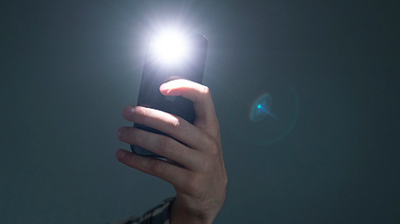Someone using a smartphone flashlight to illuminate a dark room.