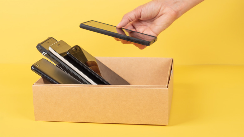 Someone taking a used phone out of a cardboard box filled with them
