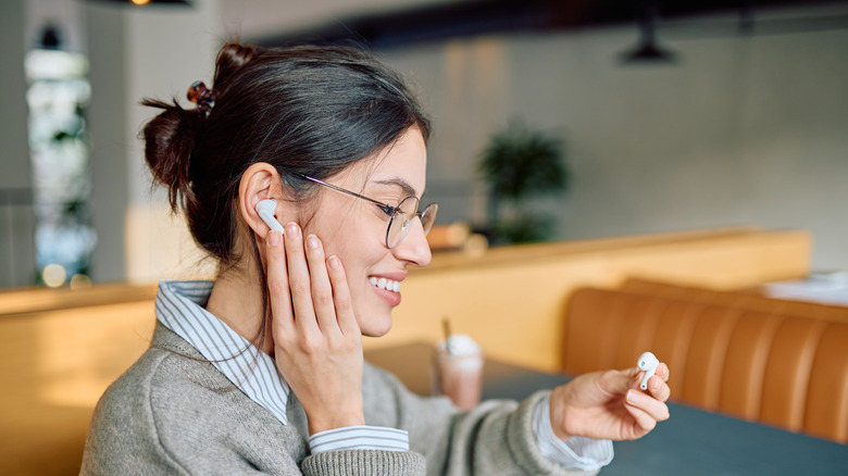 A person putting on wireless earphones in a public setting.