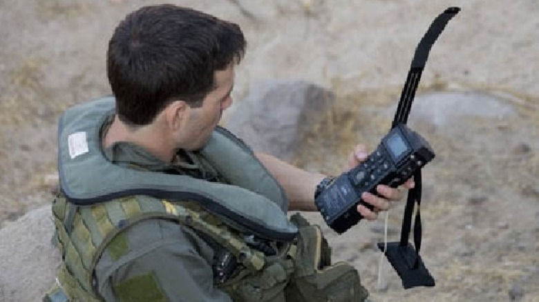 A soldier sits in a desert area, holding his handheld CSEL system