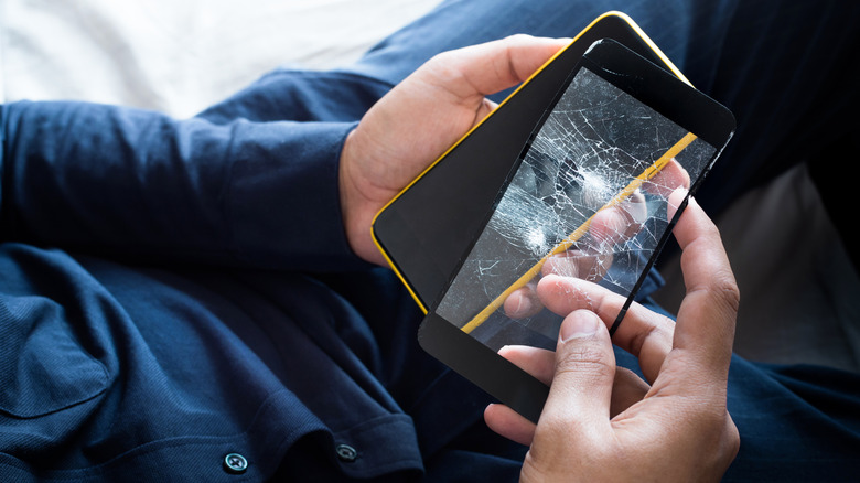Someone holding a cracked screen protector in one hand above their phone.