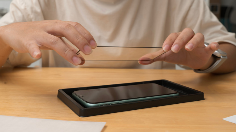 Person installing tempered glass screen protector on the front of a device.