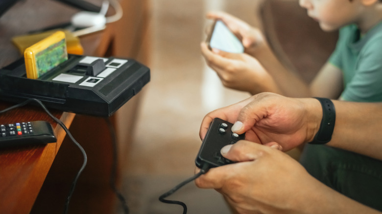 A father plays retro games while his son plays modern smartphone games
