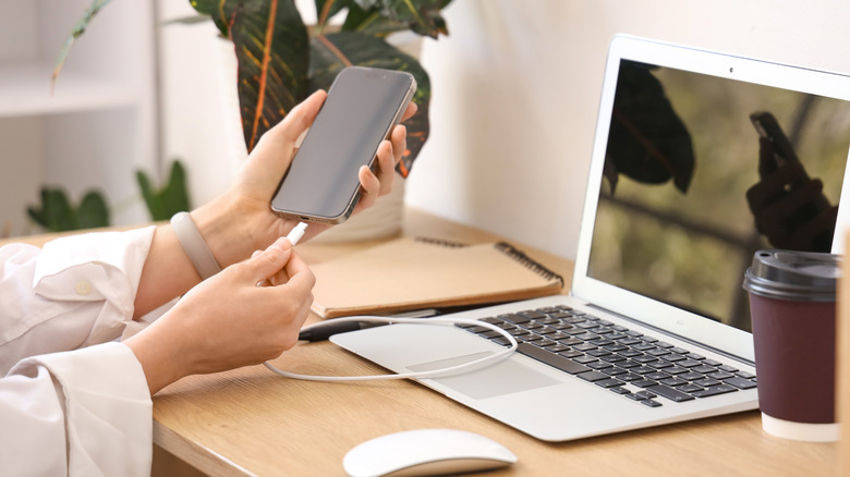 Someone in an office setting plugging in their smartphone with a laptop nearby
